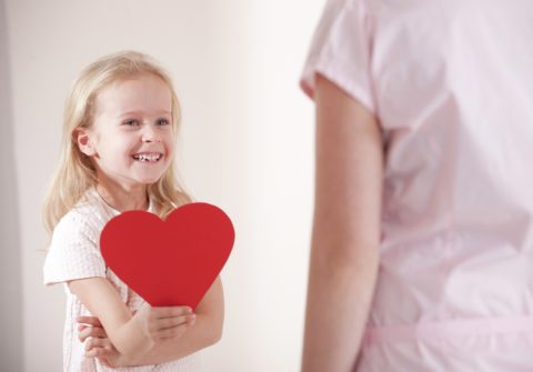 Smiling girl holding heart in front of her mother