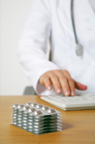 Doctor using a computer, stack of blister packs in foreground