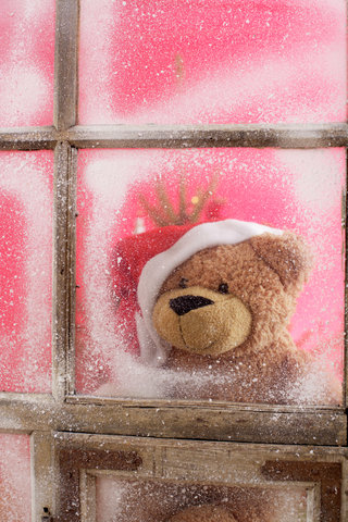 Teddy bear wearing Santa Claus hat looking out of a window