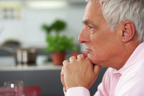 Gray-haired man with his chin resting on his hands looking thoughtfully, close-up, selective focus