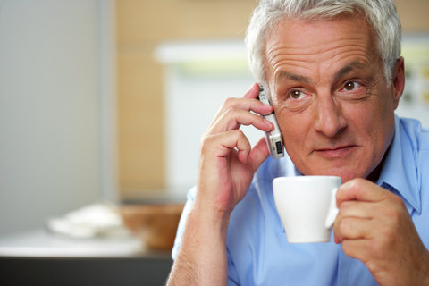 Gray-haired man phoning while having a cup of coffee, selective focus