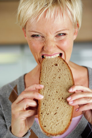 Mature woman with blond hair biting into a slice of bread, close-up