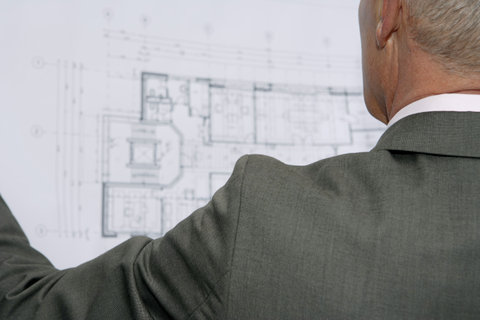 Elderly manager looking at architect's plan, rear view