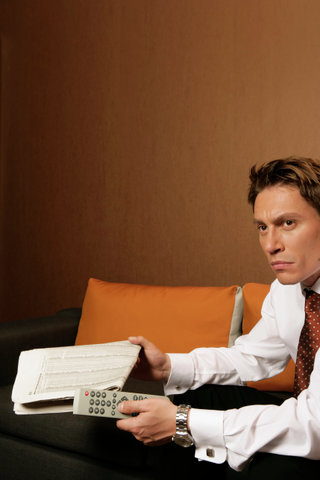 Businessman holding newspaper and remote control, watching TV