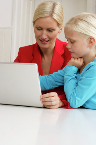 Blond girl is sitting next to her mother behind a laptop, close-up
