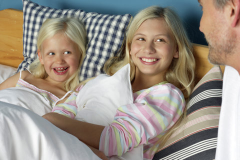 Father at the bed of his two blond daughters, close-up