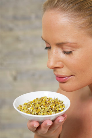 Young woman smelling at a dish of chamomile blossoms