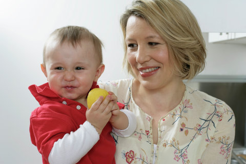 Mother carrying son on the arm, baby boy making face, holding a lemon