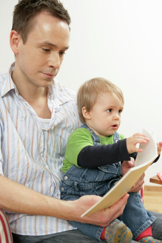 Father reading a journal, while son  sitting on his lap