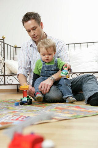 Father and son on play carpet, man rolling up baby boy's trousers