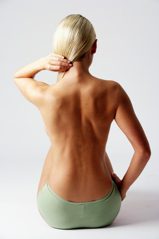 Skinny young woman holding her blonde hair, rear view