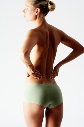 Young blonde woman only wearing a slip with her hands on hip, rear view
