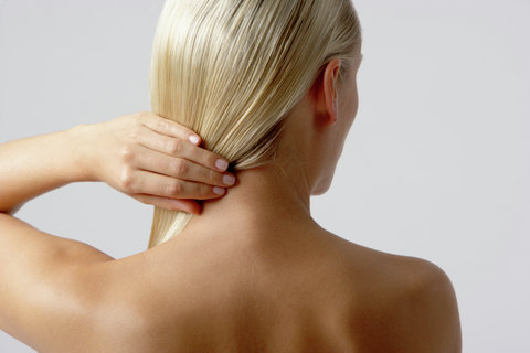 Skinny young woman holding her blonde hair, rear view