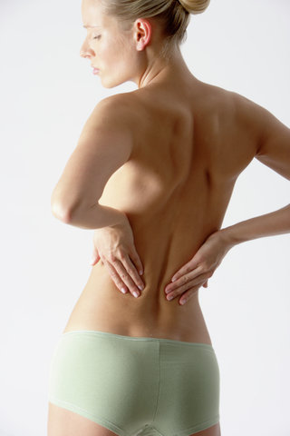 Young blonde woman only wearing a slip with her hands on her back, rear view