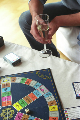 Man holding a Champagne Glass and a Board Game laying on a Table (cropped)