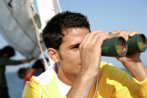 Man on a sailboat looking through binoculars