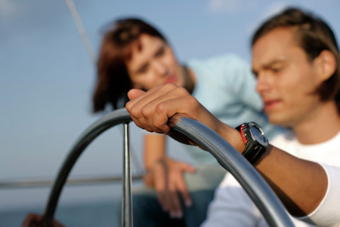 Man at steering wheel of a sailboat, woman standing behind him