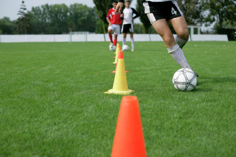 Soccer player running with football slalom around pylons