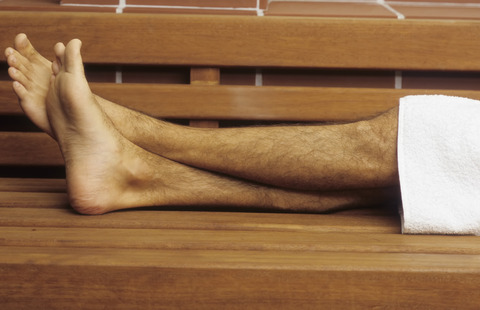 Naked Legs of a Man with a Towel lying on a wooden Bench - Sauna - Relaxation - Wellness