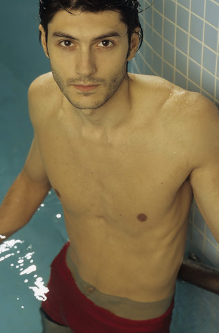 Darkhaired Man leaning against the wall of a Swimming Pool - Baths - Leisure Time