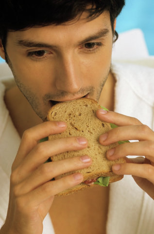 Darkhaired Man in a Bathrobe biting into a Sandwich - Snack - Foodstuff