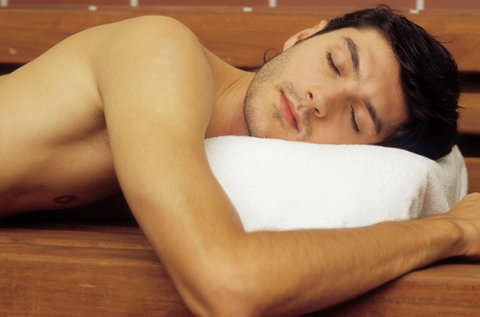 Darkhaired Man with naked Torso lies on a wooden Bench snoozing - Sauna - Relaxation - Wellness